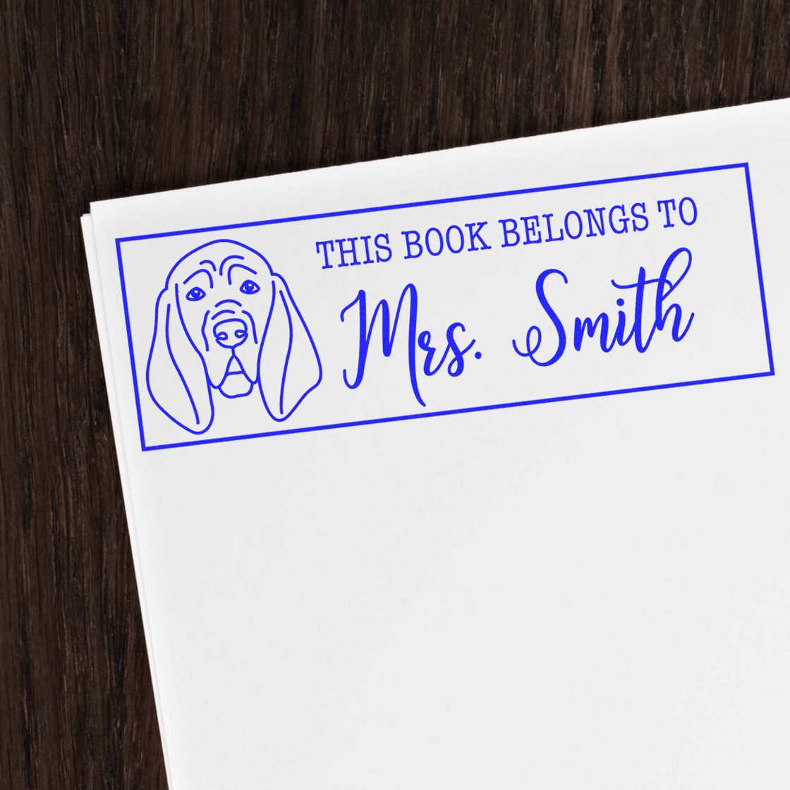 Blue personalized book stamp and seal with dog outline and This Book Belongs to Mrs. Smith in blue on white paper.