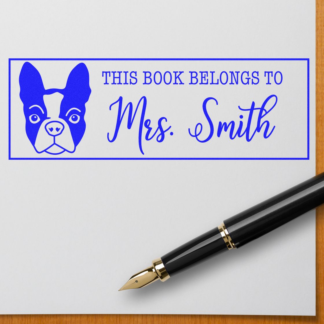 Blue custom book ownership stamp with dog and Mrs. Smith on white paper, beside a black-and-gold fountain pen.