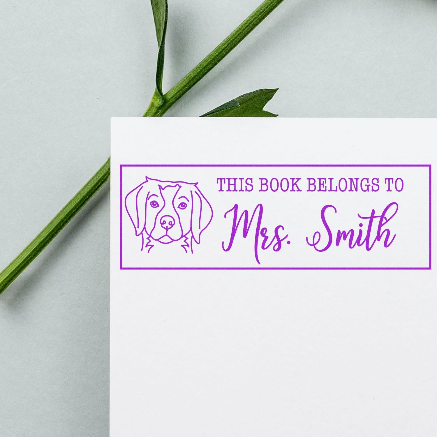 Purple custom book stamp with dog outline and This book belongs to Mrs. Smith on white paper.