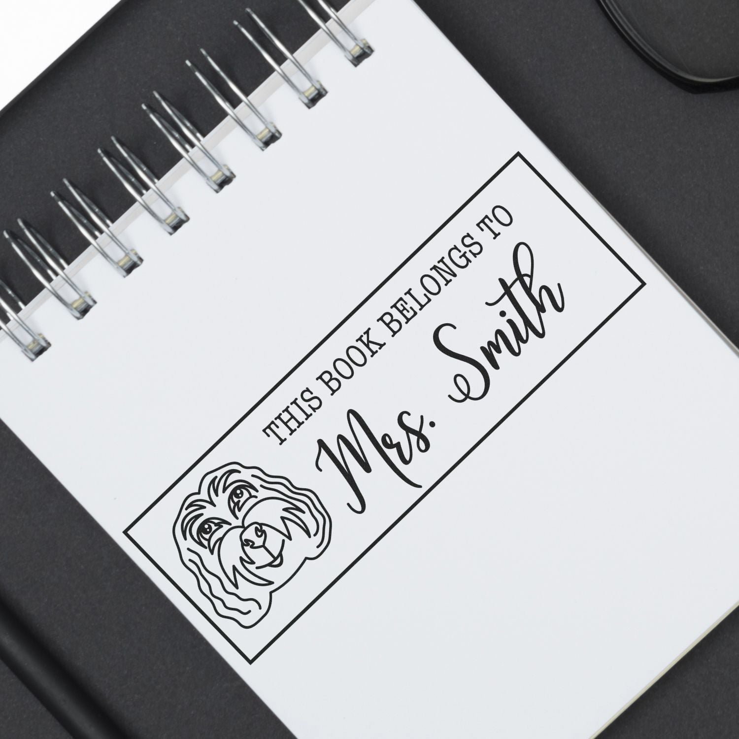 Black custom stamp seal for Mrs. Smith with dog portrait on a white spiral notebook.