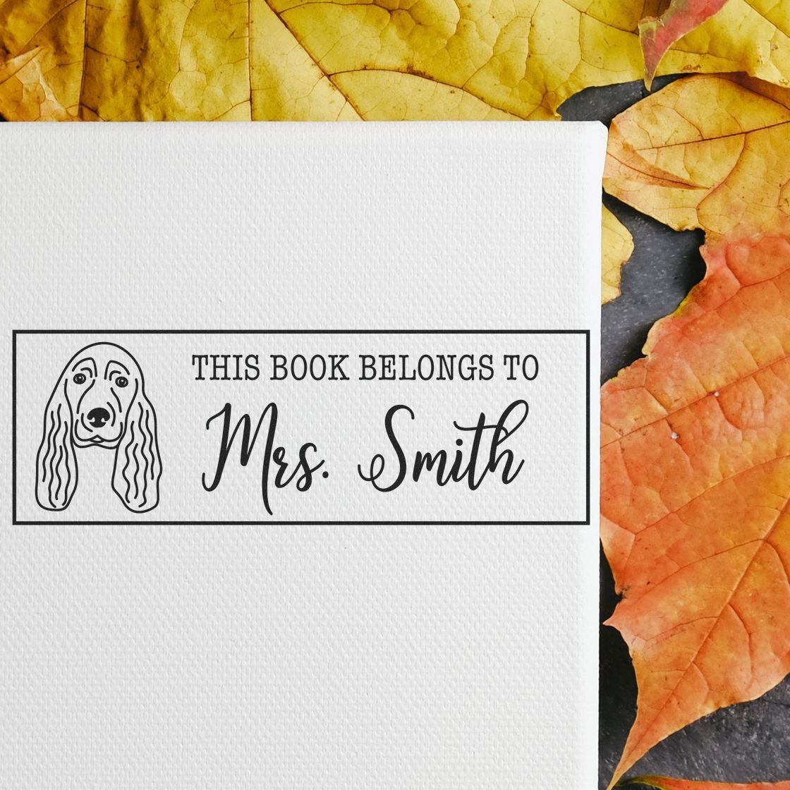 White book ownership stamp with black dog seal and This Book Belongs to Mrs. Smith text on textured paper, against yellow-orange leaves.