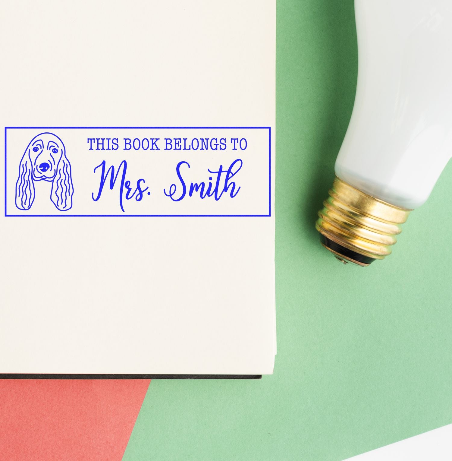 Blue personalized book stamp with dog icon and This Book Belongs to Mrs. Smith, beside a white-and-gold seal applicator on green.