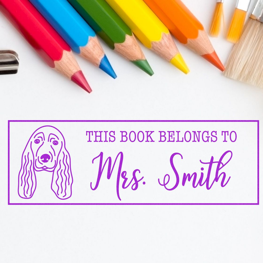 Purple custom book stamp and seal reading This Book Belongs to Mrs. Smith, with dog outline and colorful pencils.