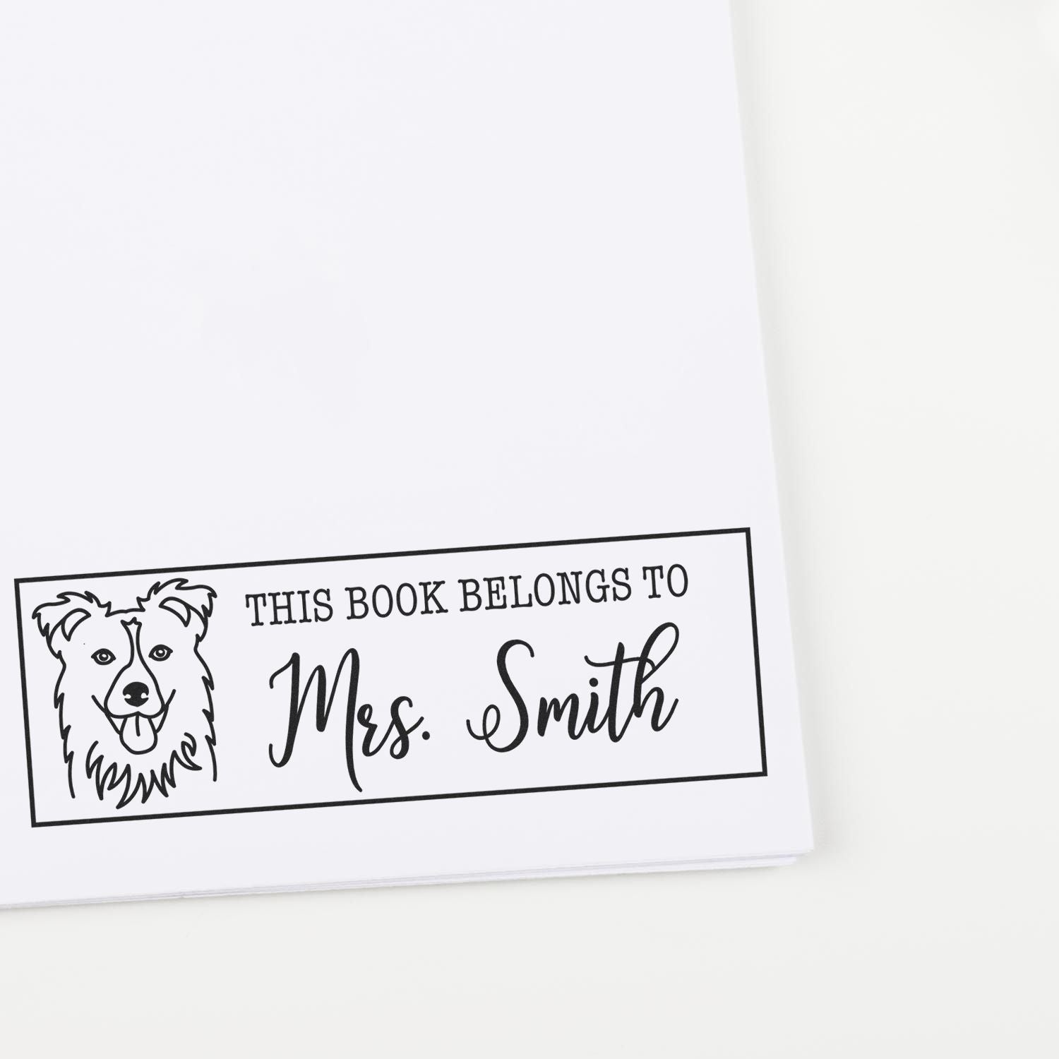 Black custom book stamp with dog illustration and This book belongs to Mrs. Smith on white paper.