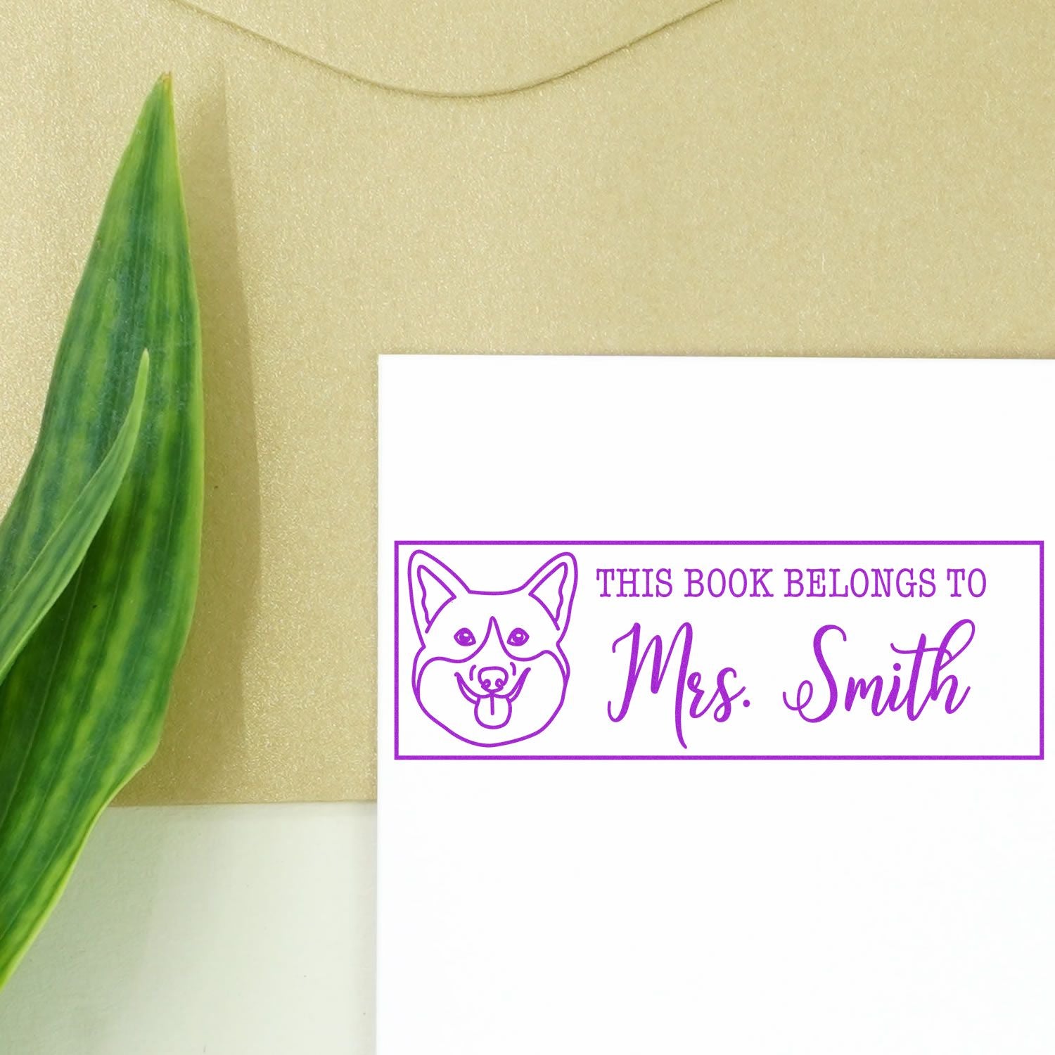 Purple custom book stamp and seal with dog illustration and Mrs. Smith text on white card, beige background, green leaf.