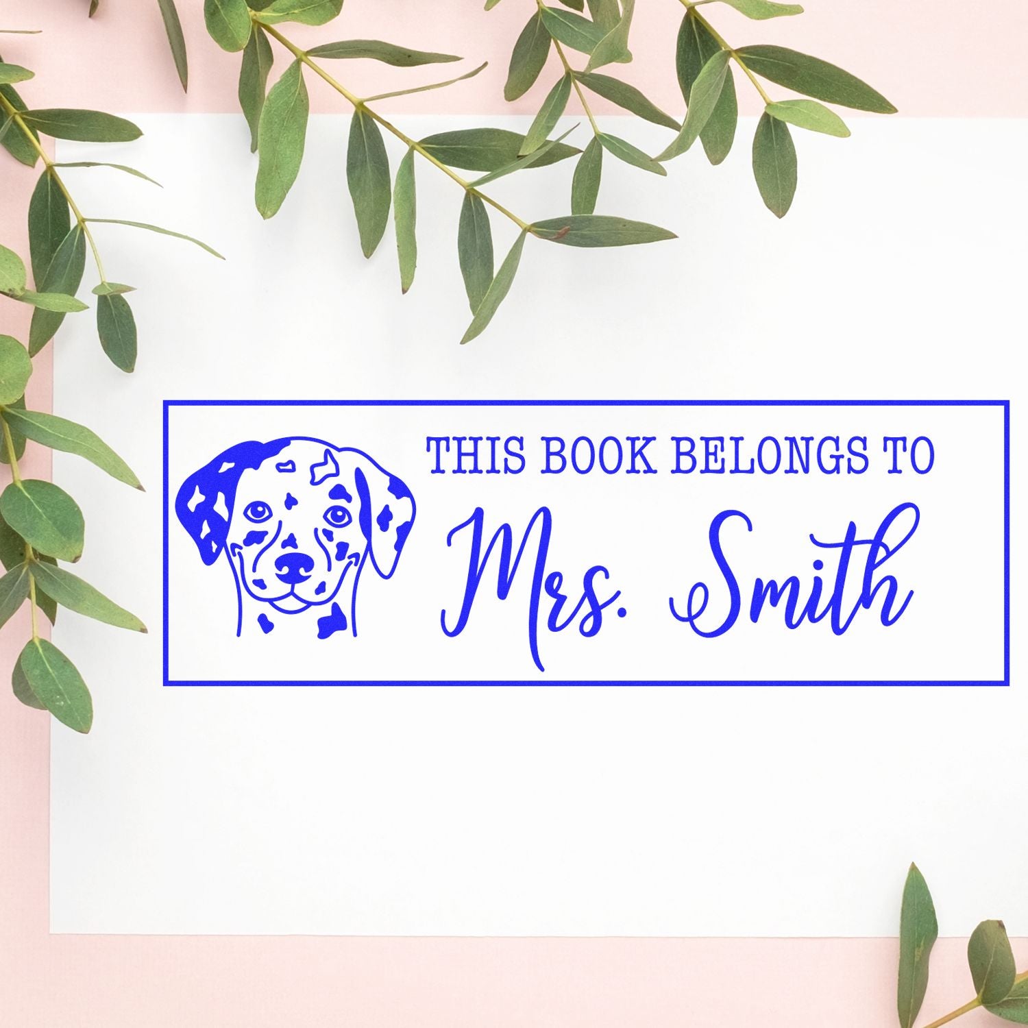 Blue custom book stamp seal with dog illustration and "This Book Belongs to Mrs. Smith" on white card with green leaves.