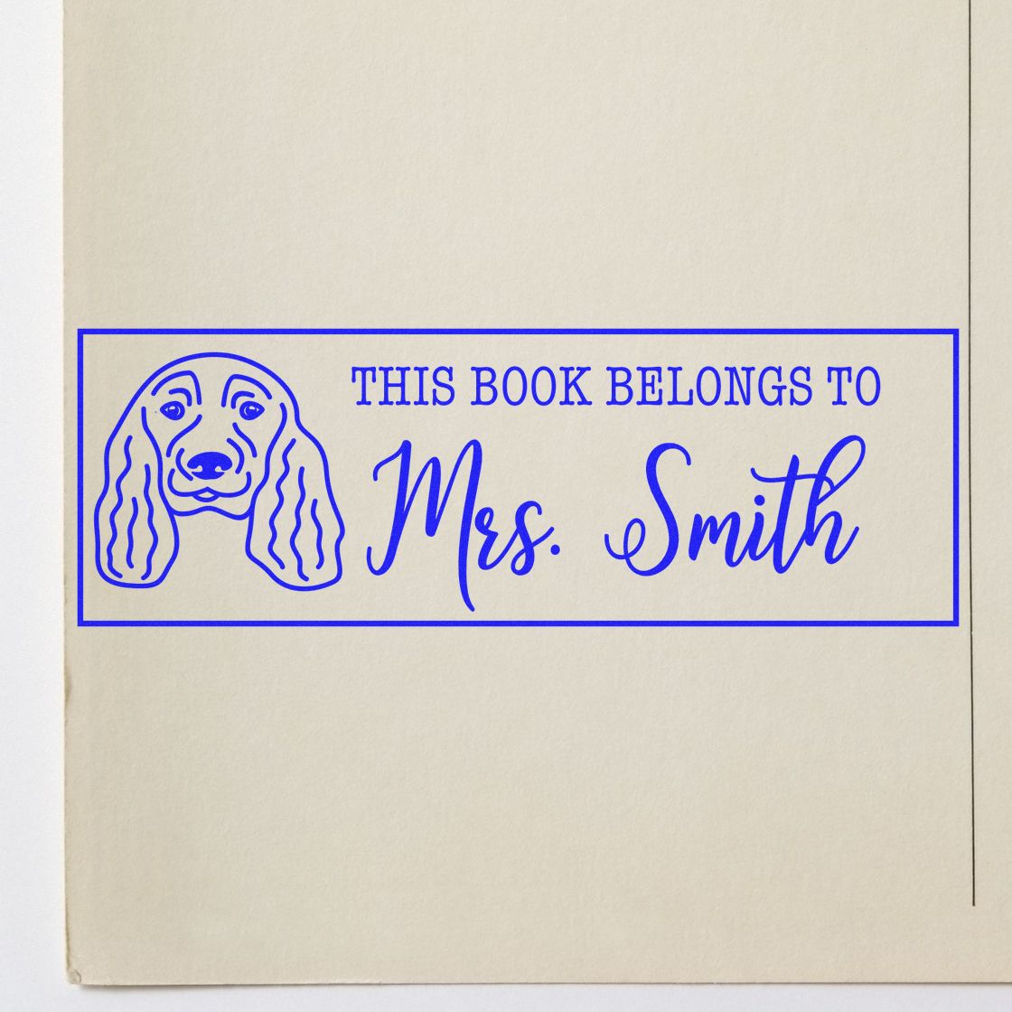 Blue custom book stamp with dog illustration and This Book Belongs to Mrs. Smith on beige paper.