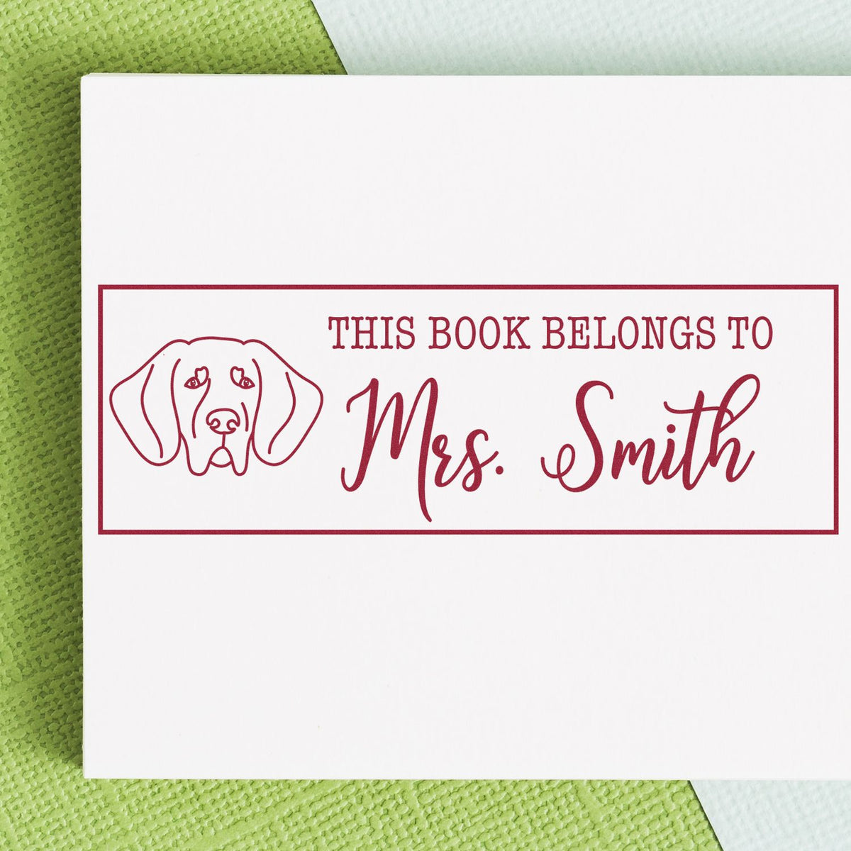 Custom maroon book stamp and seal with dog outline and This Book Belongs to Mrs. Smith on white card.