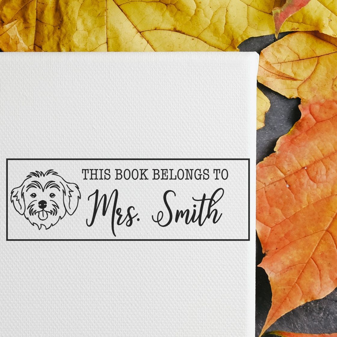 Black custom book stamp seal with dog icon and This Book Belongs to Mrs. Smith on white paper, framed by autumn leaves.