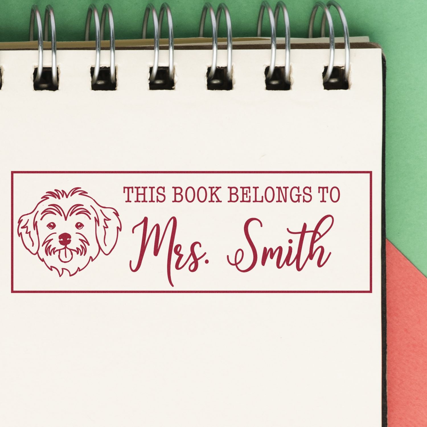 Red custom bookplate stamp and seal with dog icon and This book belongs to Mrs. Smith on a white spiral notebook.