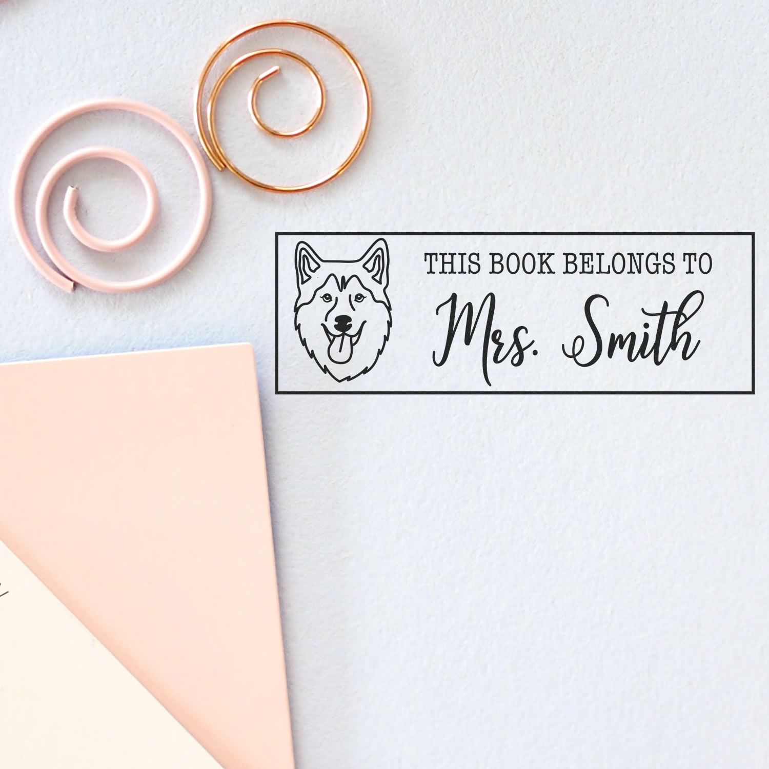 Custom book stamp and seal for Mrs. Smith, black husky design, with pink and gold spiral clips on a white background.