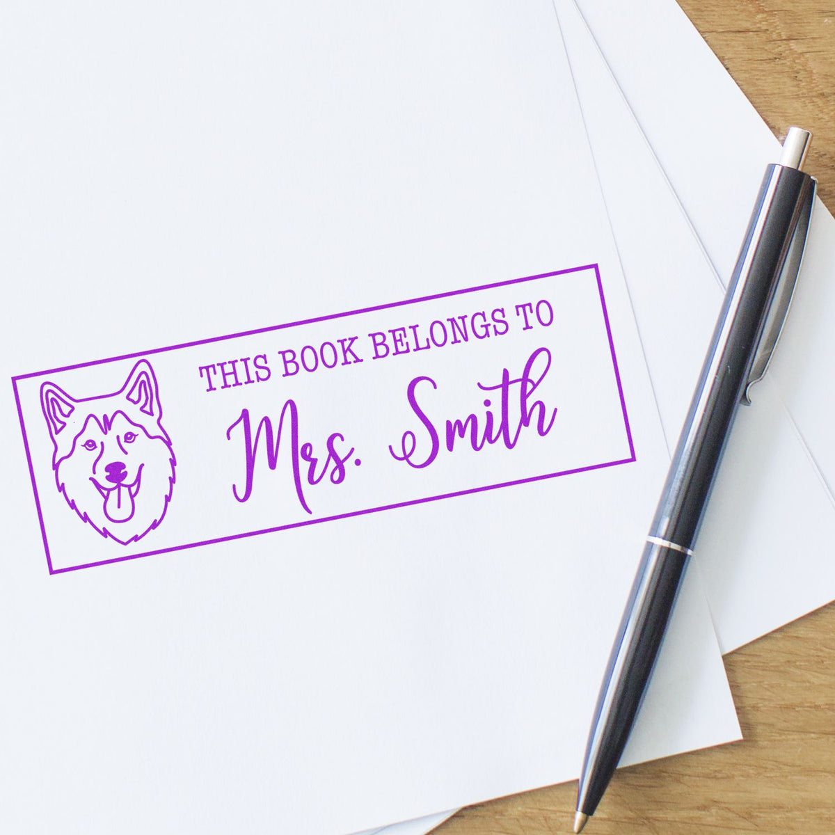 Purple book stamp/seal with dog icon and Mrs. Smith text on white paper, beside a black-and-silver pen.