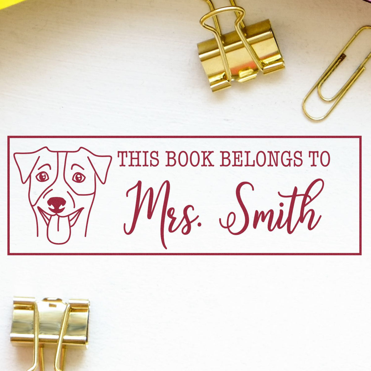 Red custom book stamp and seal with dog illustration, This book belongs to Mrs. Smith, on white paper with gold binder clips.