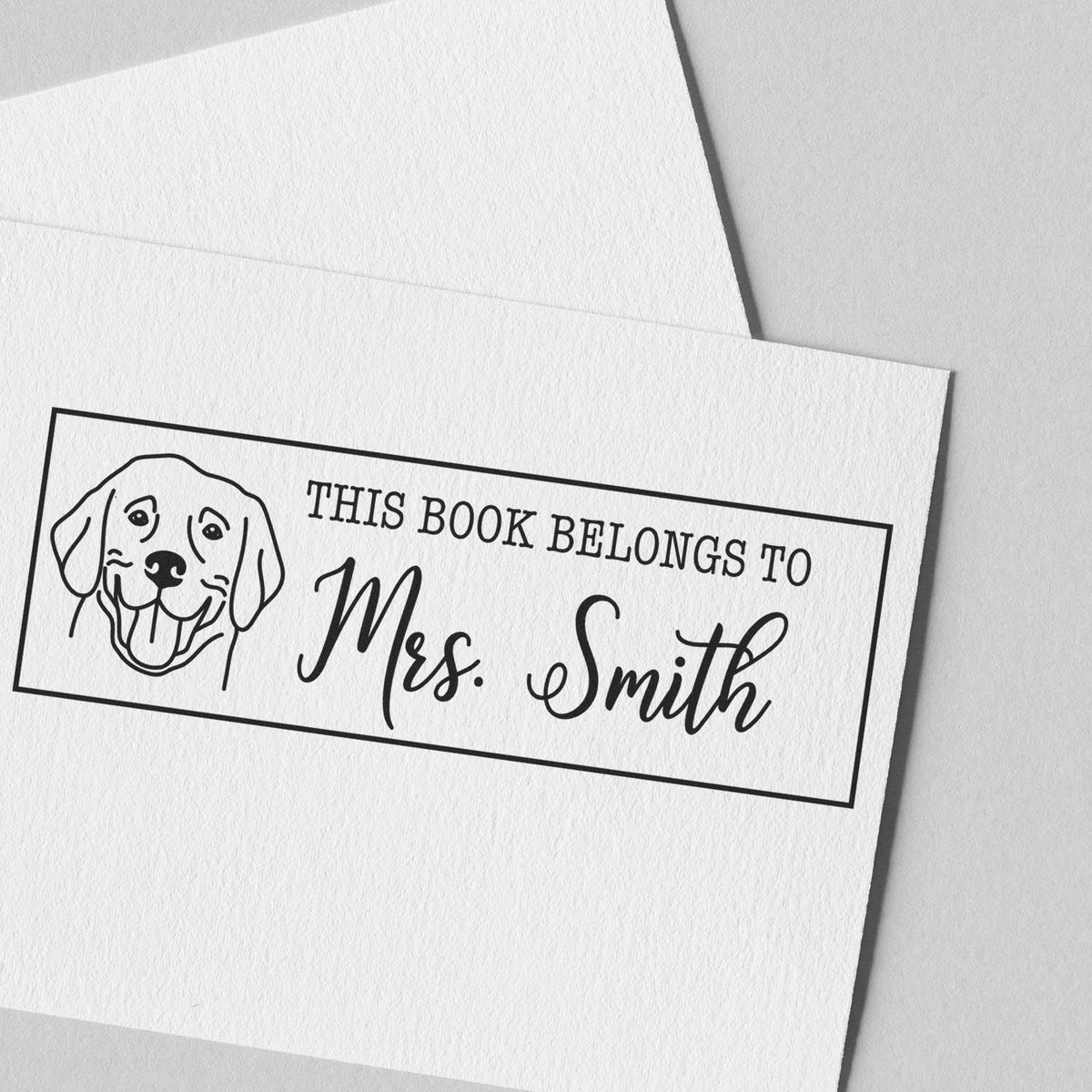 Black personalized book stamp and seal with dog illustration and This book belongs to Mrs. Smith on white textured paper.