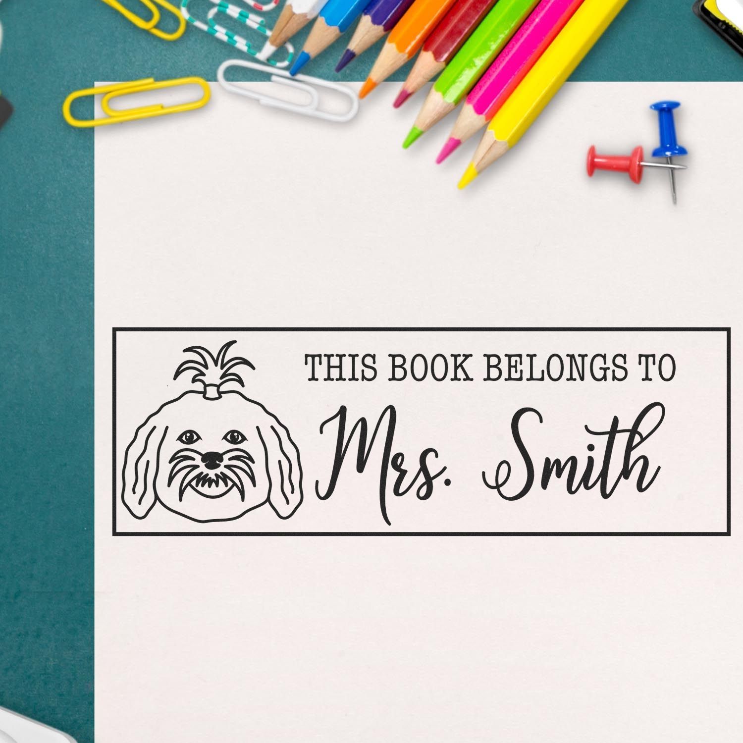 Custom book stamp and seal with dog graphic and This Book Belongs to Mrs. Smith, on white paper with colorful pencils.