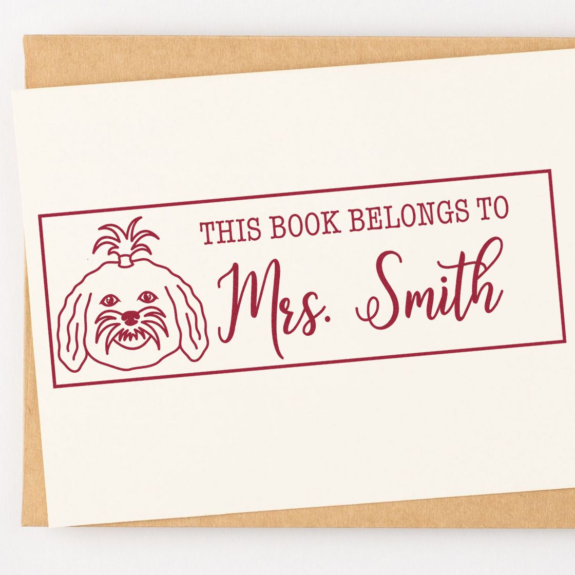 Burgundy custom book plate stamp with dog illustration and Mrs. Smith text on cream card over kraft envelope.