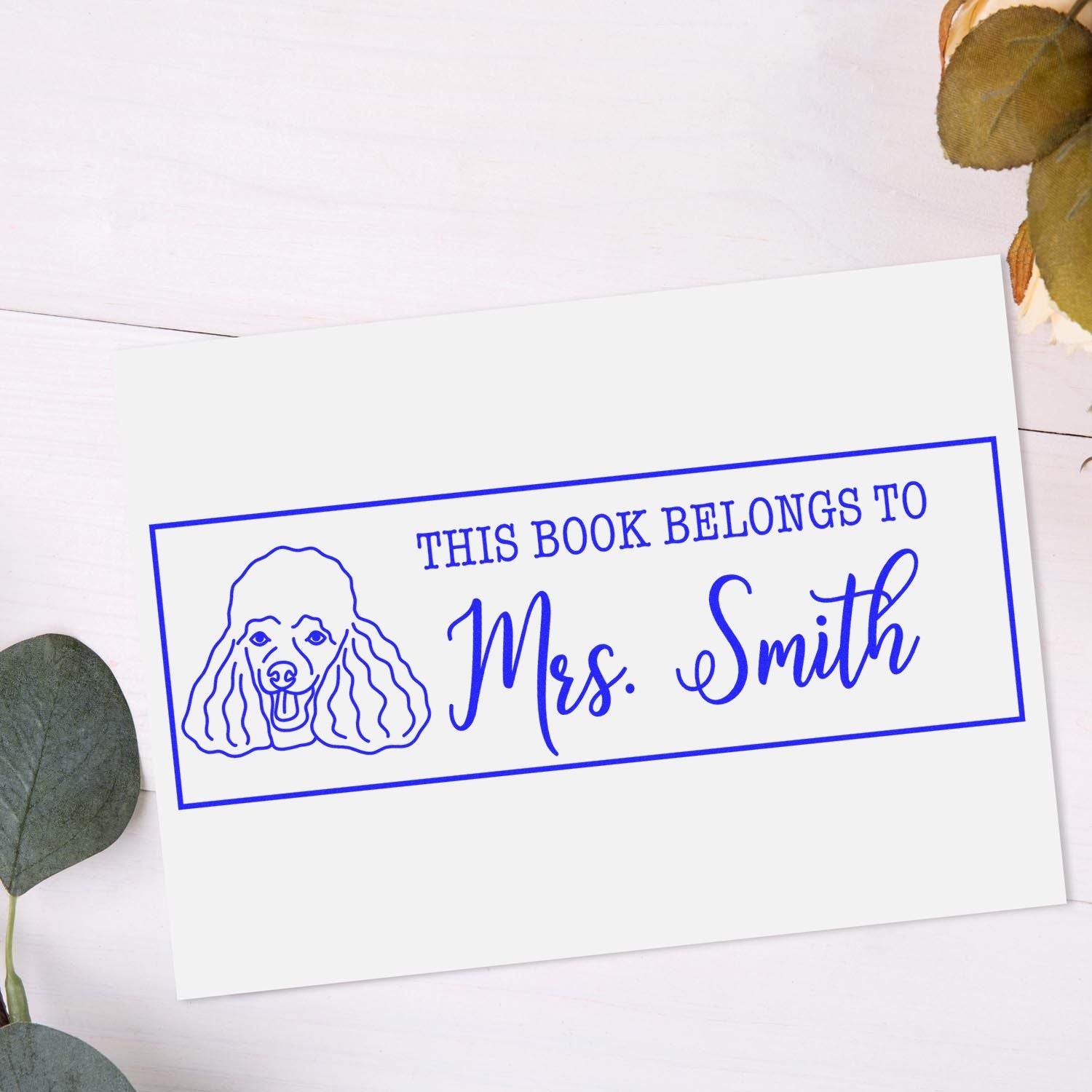 Blue custom book stamp and seal with poodle outline and This book belongs to Mrs. Smith on white card.