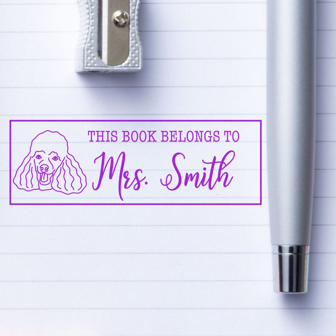 Purple custom book stamp and seal reading This Book Belongs to Mrs. Smith with a poodle on lined paper.