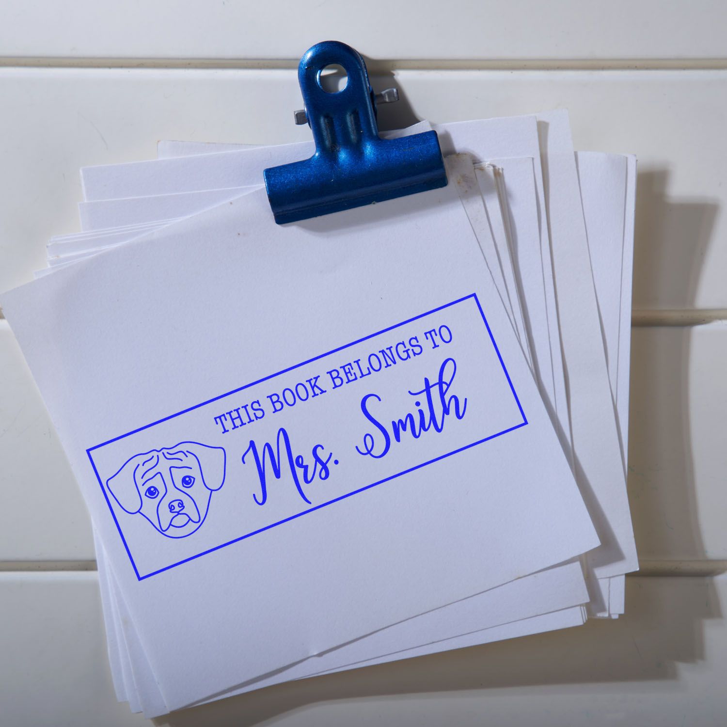 Blue bookplate stamp and dog seal on white cards, clipped with a blue binder clip.