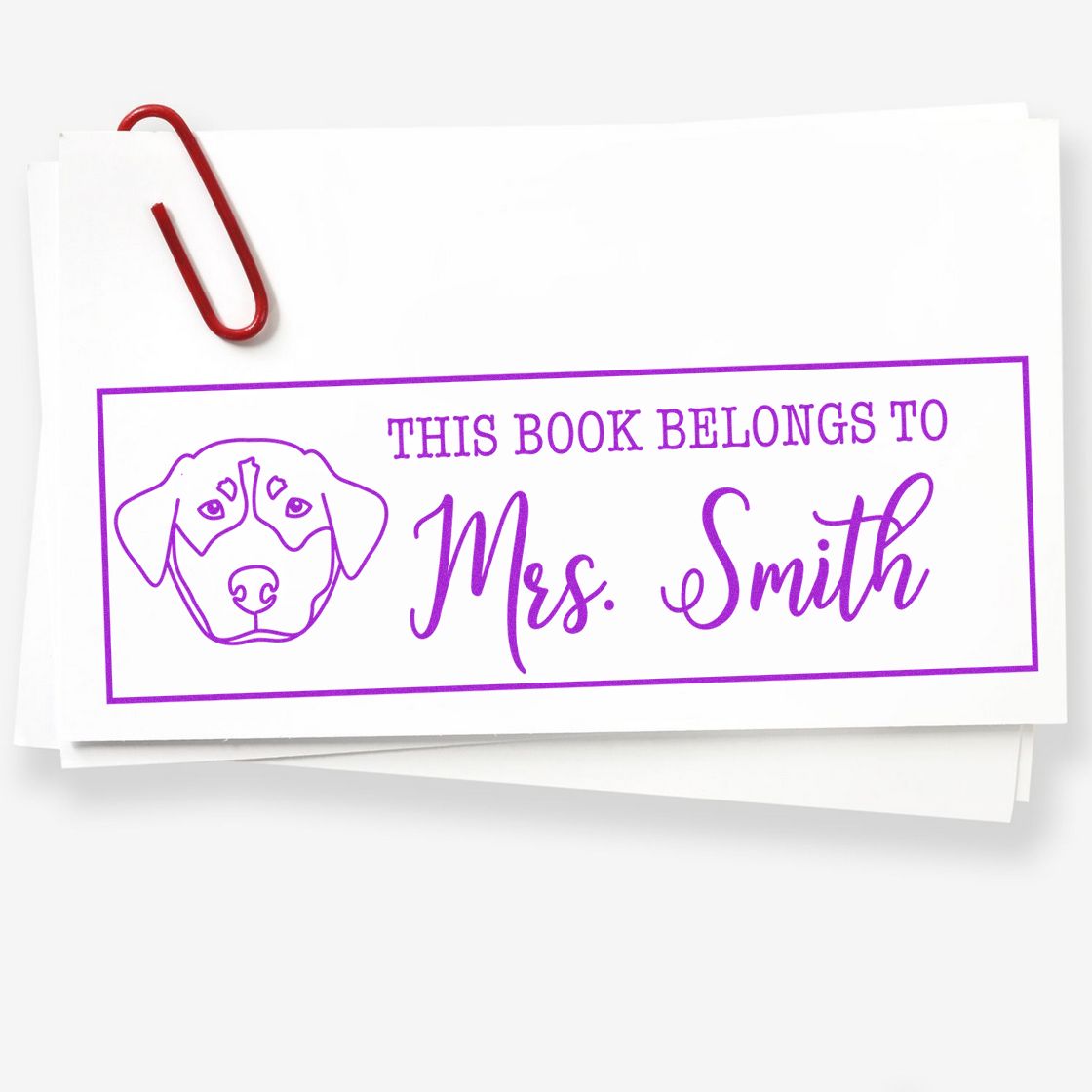 Purple custom book stamp and seal with dog icon and This Book Belongs to Mrs. Smith on white paper, clipped with a red paperclip.