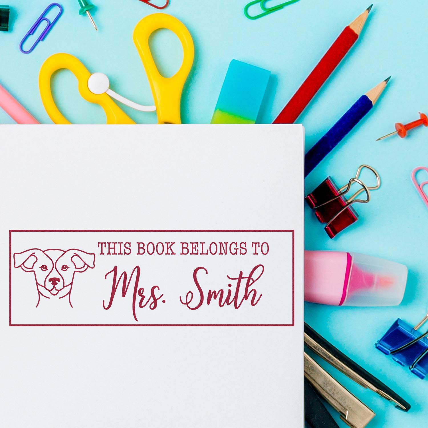 Custom maroon book stamp seal for Mrs. Smith on white paper, surrounded by colorful stationery tools.