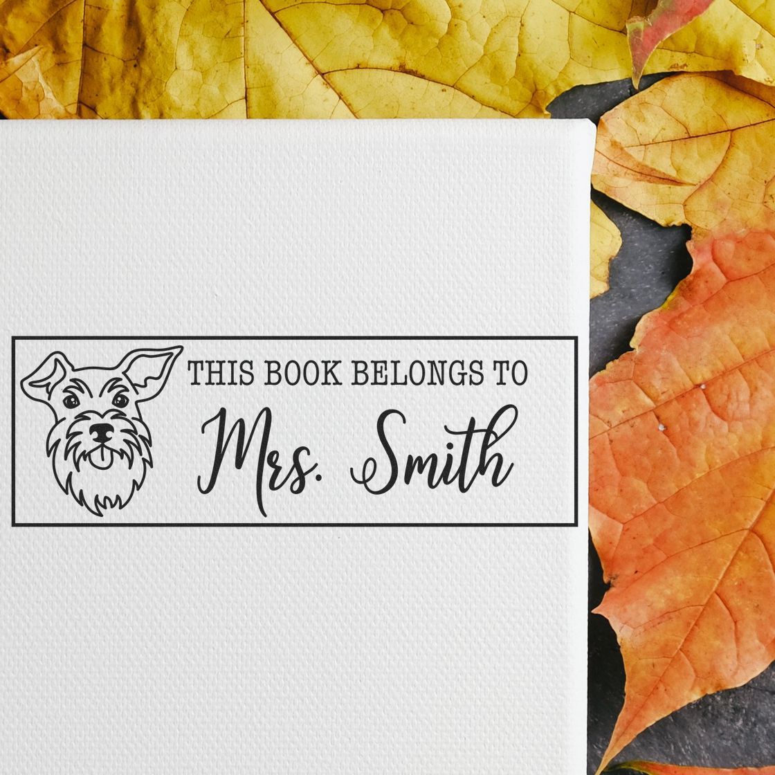 Black custom bookplate stamp seal with dog illustration and Mrs. Smith text on white textured paper, against orange and yellow leaves.