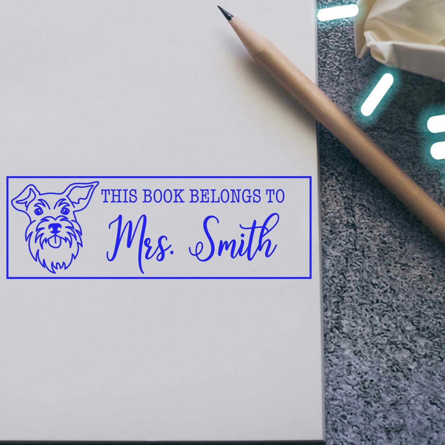 Blue custom book ownership stamp and seal with dog illustration and This book belongs to Mrs. Smith on white paper.