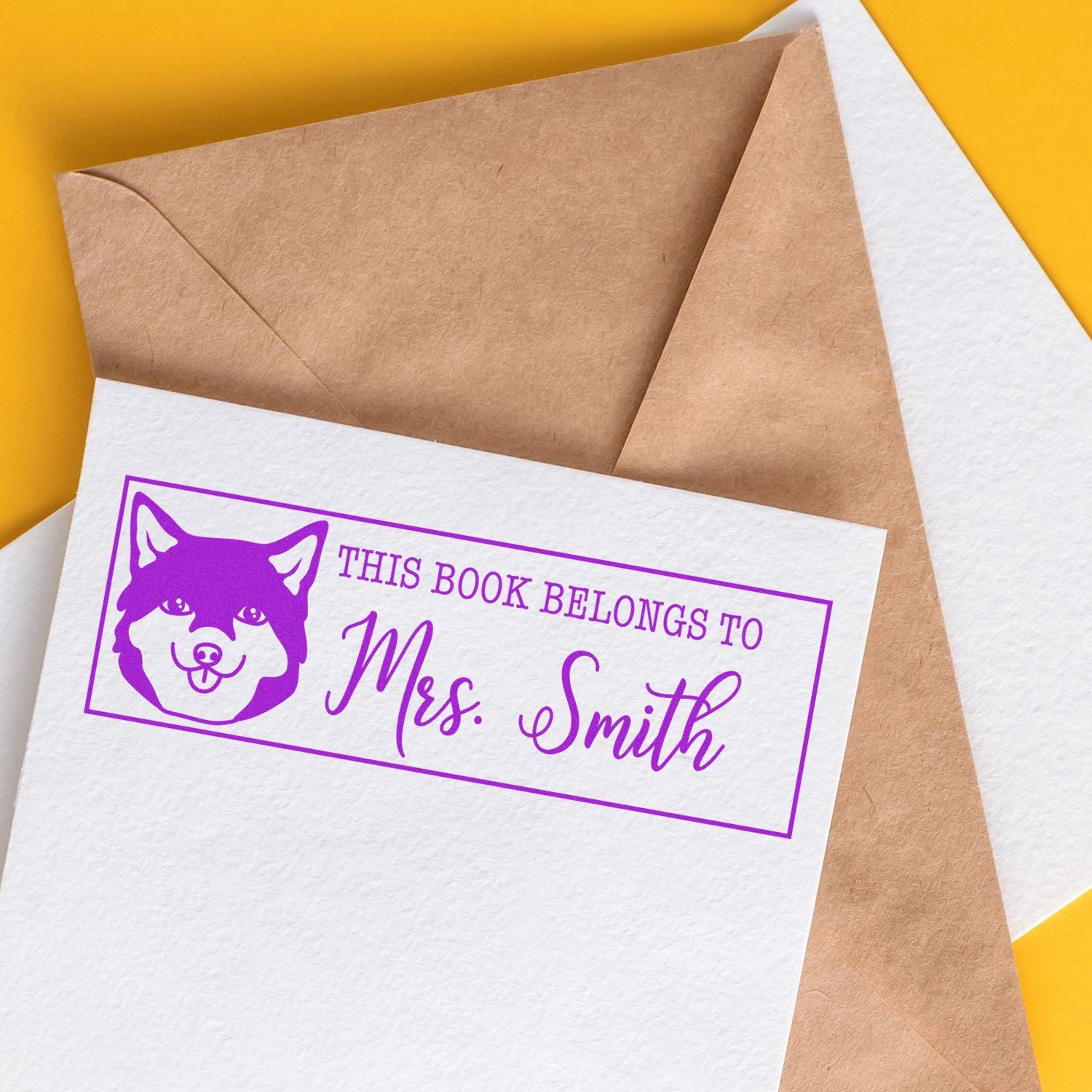 Purple custom book stamp and seal with dog icon on white paper, beside kraft envelopes on a bright yellow background.