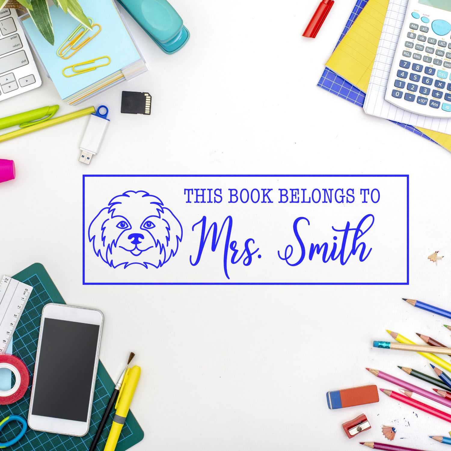 Blue custom book stamp seal with dog icon and This Book Belongs to Mrs. Smith on a white desk.