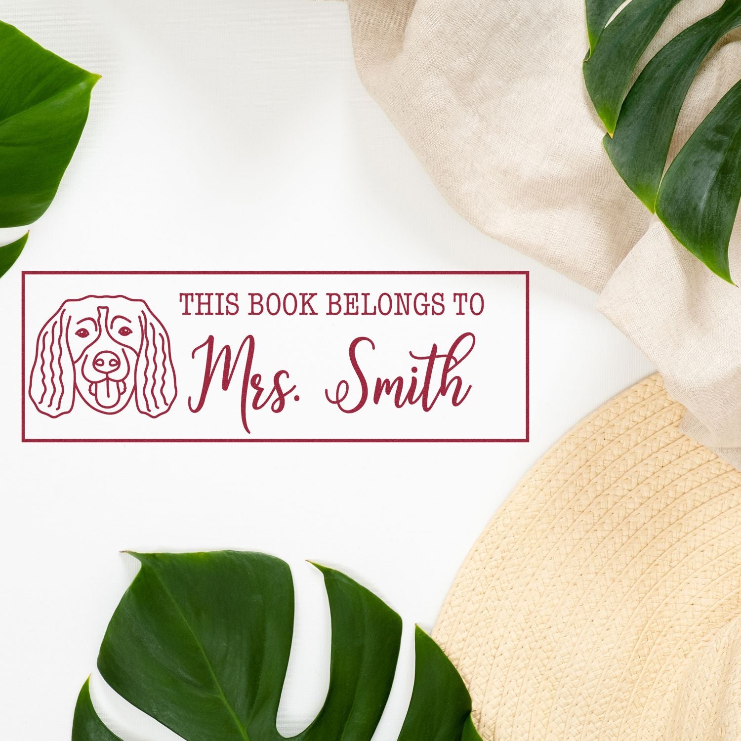 Maroon custom book stamp and seal with dog outline, This Book Belongs to Mrs. Smith, on white with green leaves.