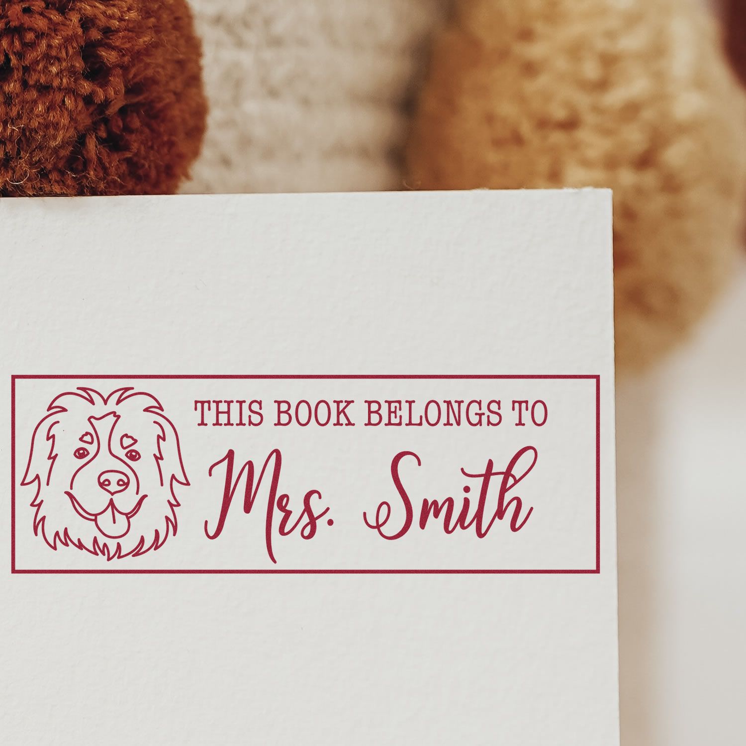 Red custom book ownership stamp with dog seal, reading This Book Belongs to Mrs. Smith on white paper.
