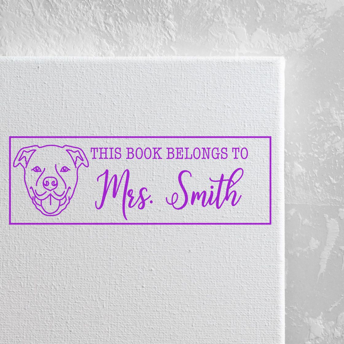 Purple personalized book stamp with dog seal and This Book Belongs to Mrs. Smith on a white textured background.