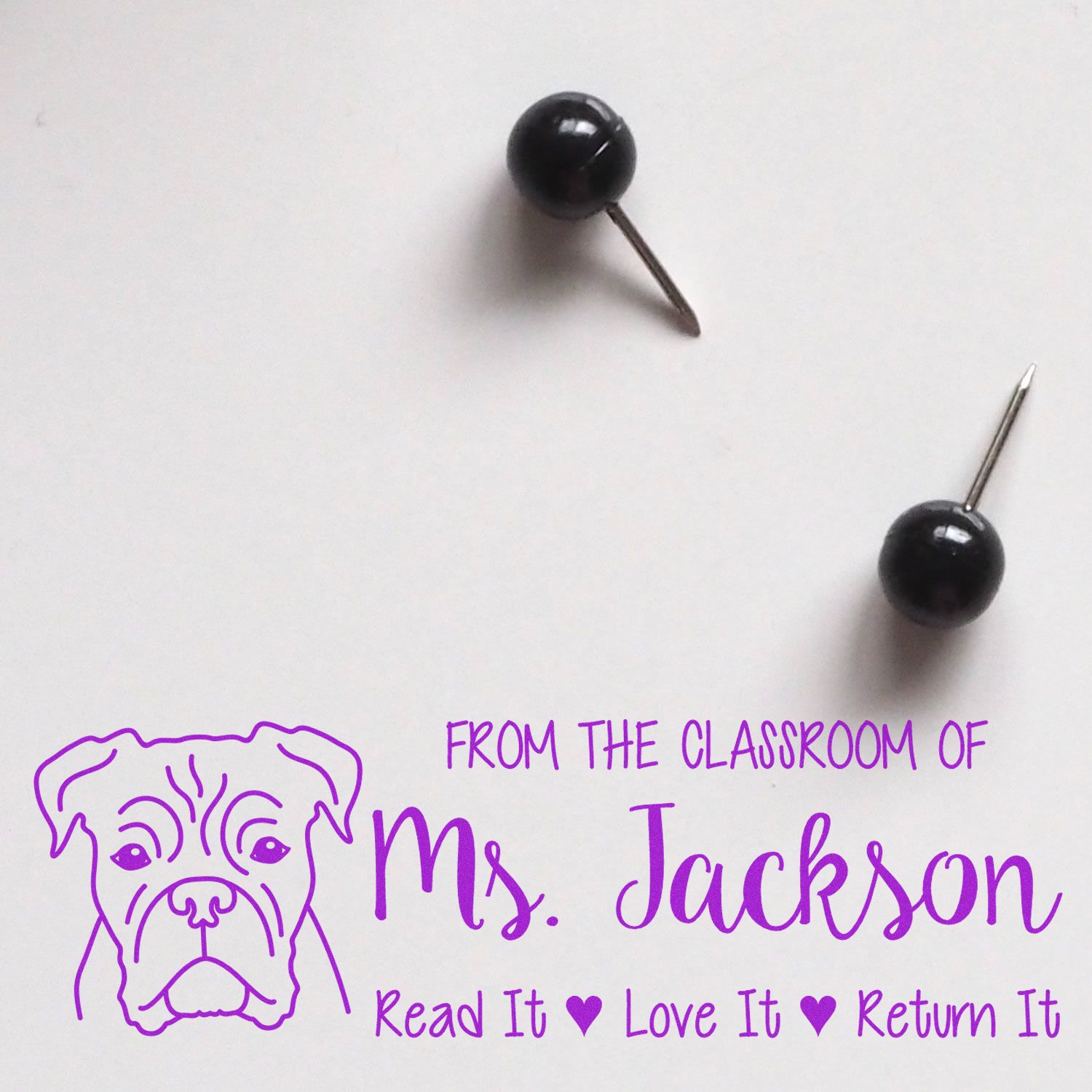 Black push pins beside a purple custom stamp and seal with dog logo, Ms. Jackson, and Read It Love It Return It.