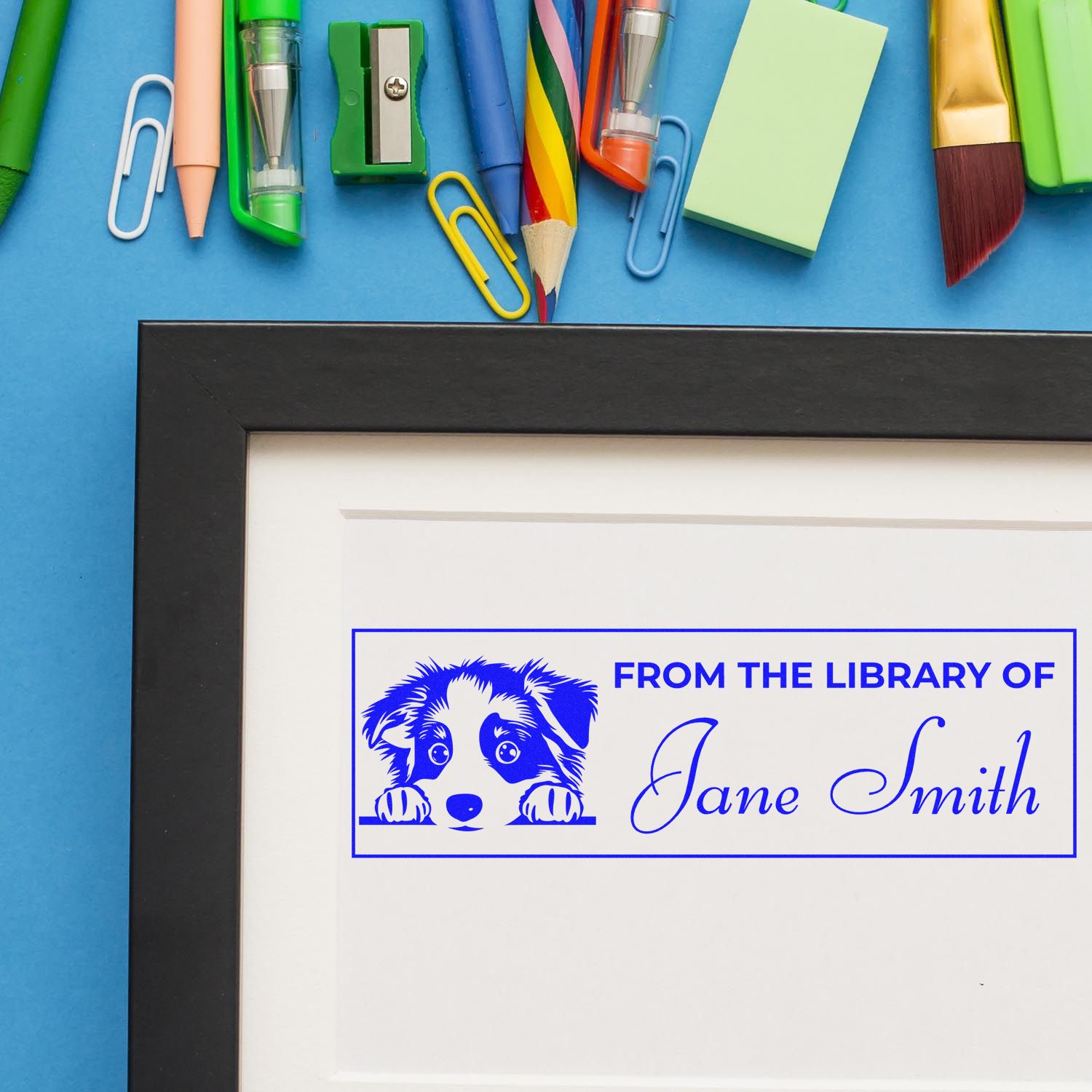 Blue custom library stamp and seal with dog graphic and Jane Smith name in a black frame, on a blue background with colorful stationery.