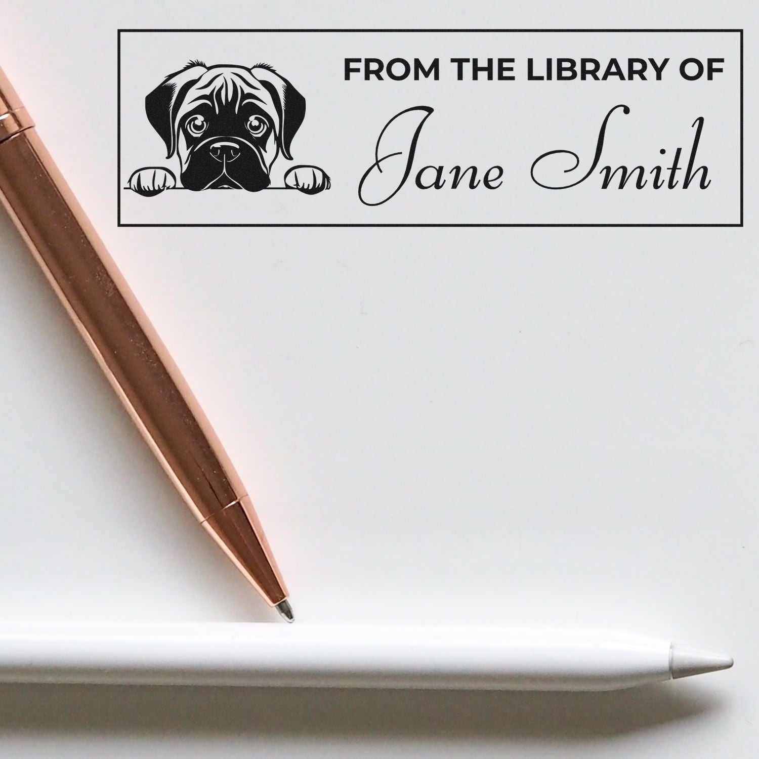 Black custom library stamp with dog illustration and Jane Smith, beside rose gold and white pens on a white background.