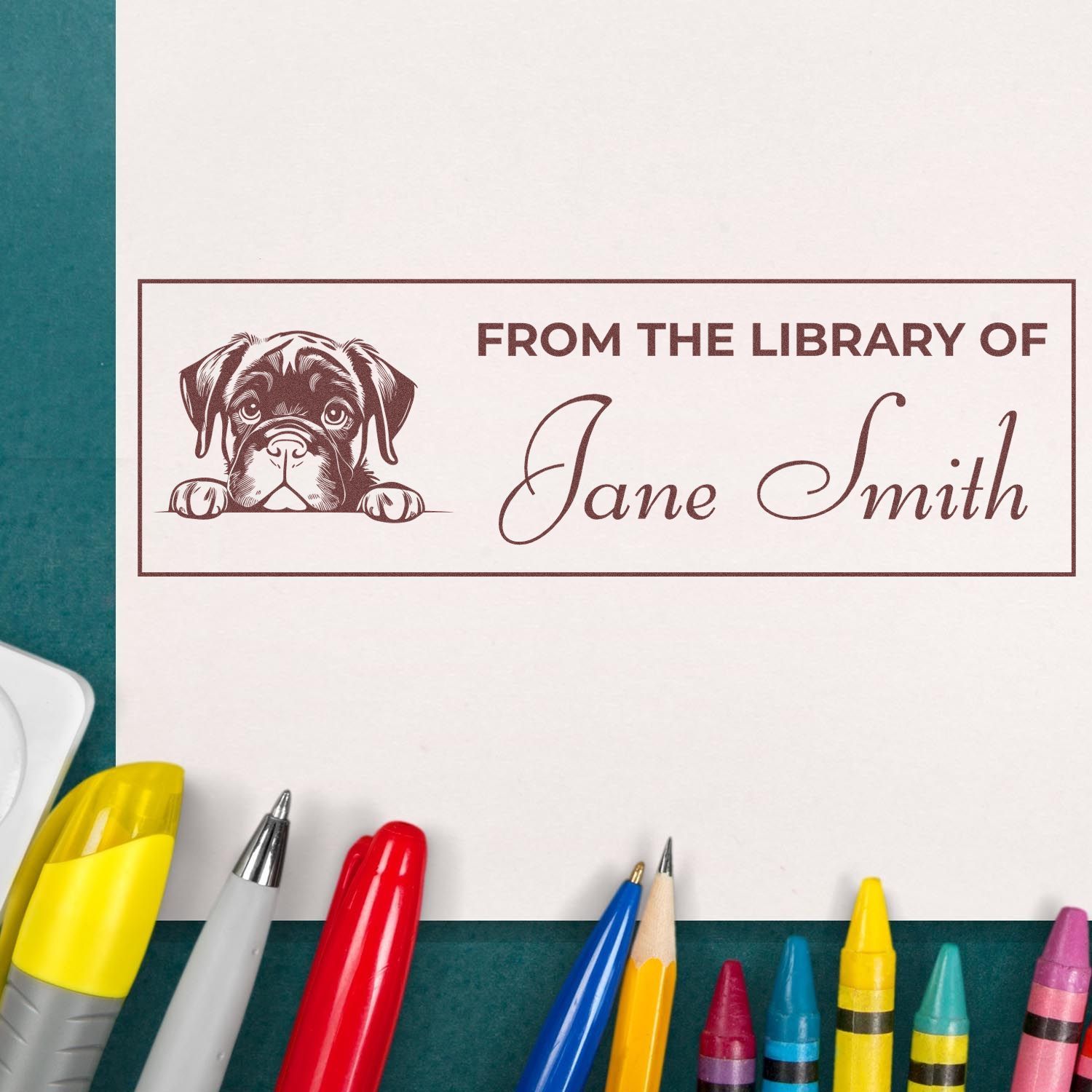 Brown custom library book stamp with dog illustration and Jane Smith text on white paper, surrounded by colorful pens.