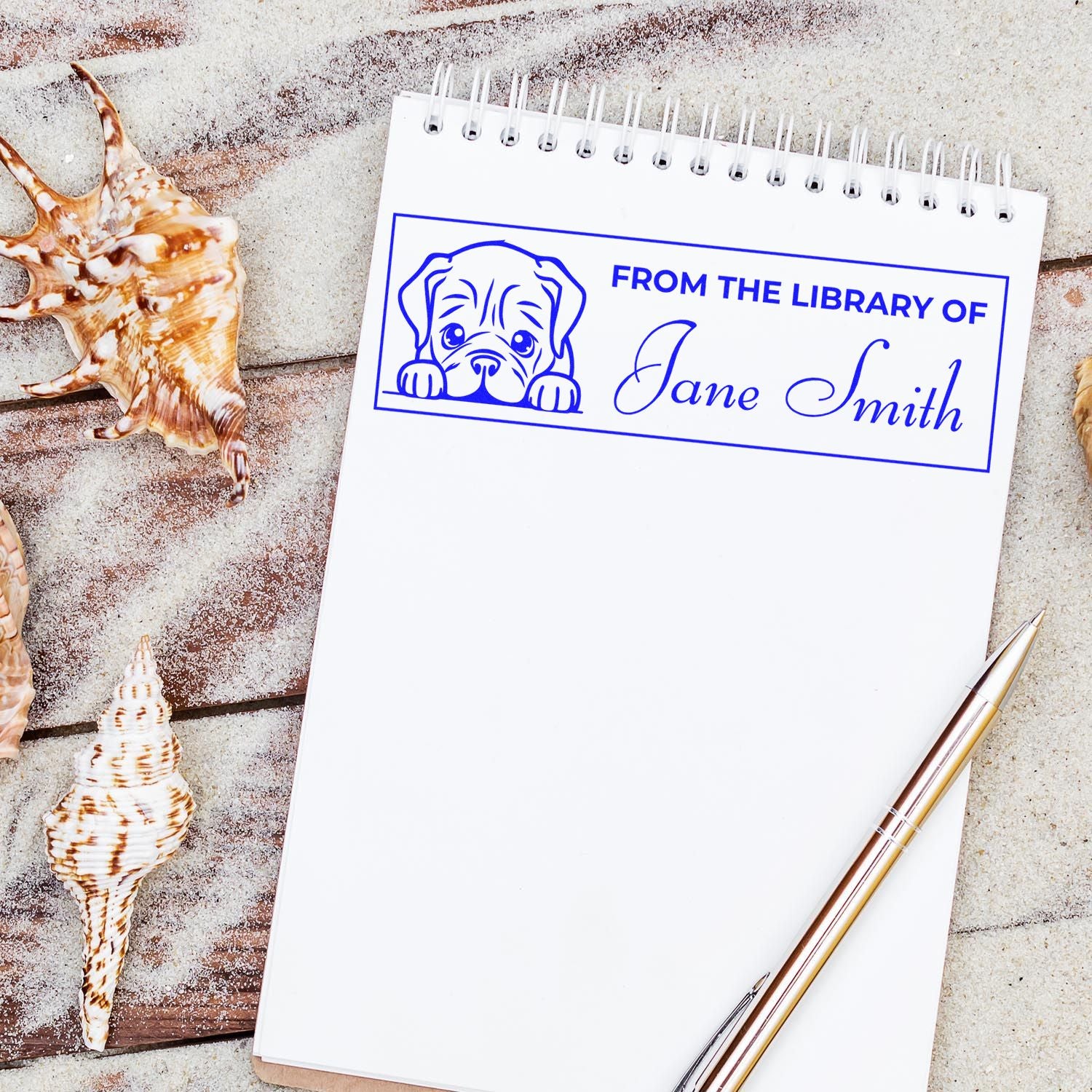 White spiral notepad with blue custom library stamp, dog icon, Jane Smith text, on seashell background with pen.
