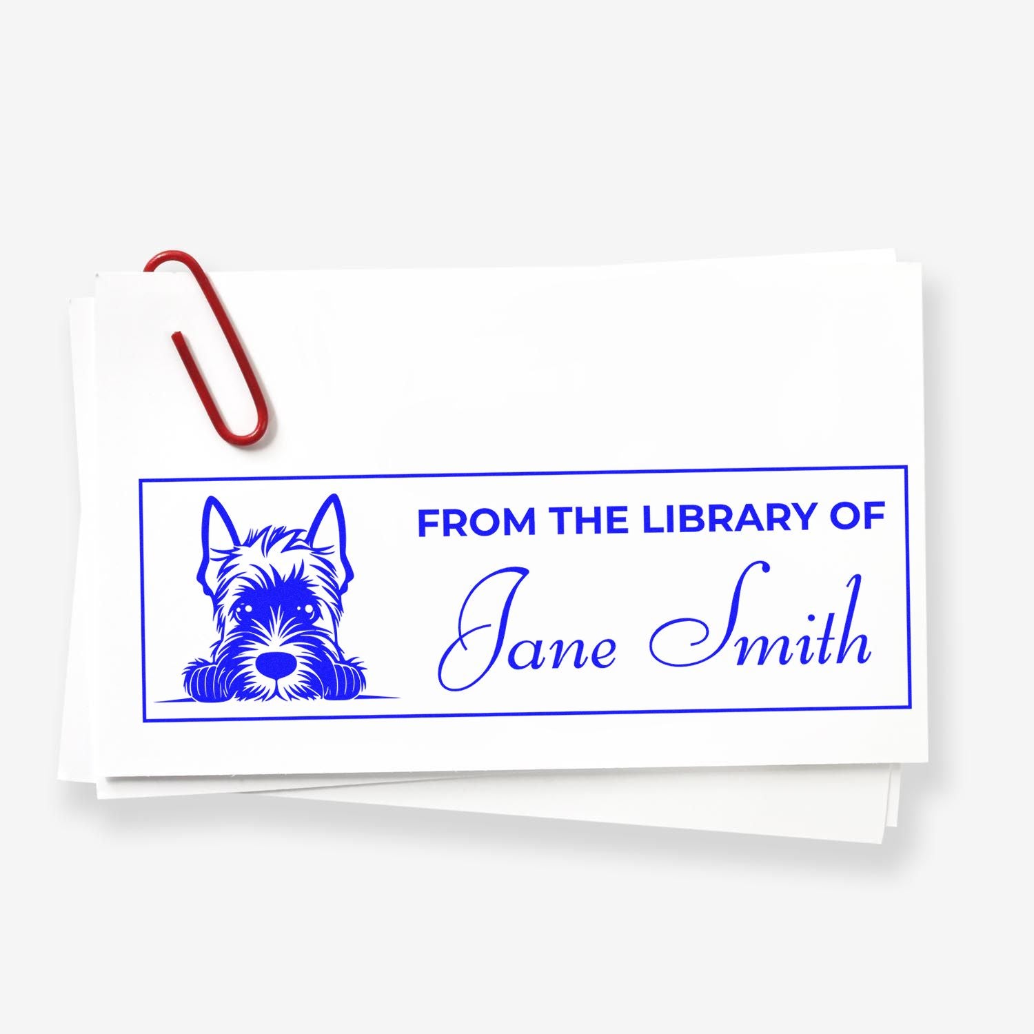 Blue custom library book stamp with dog illustration, Jane Smith text, on white paper clipped with a red paperclip.