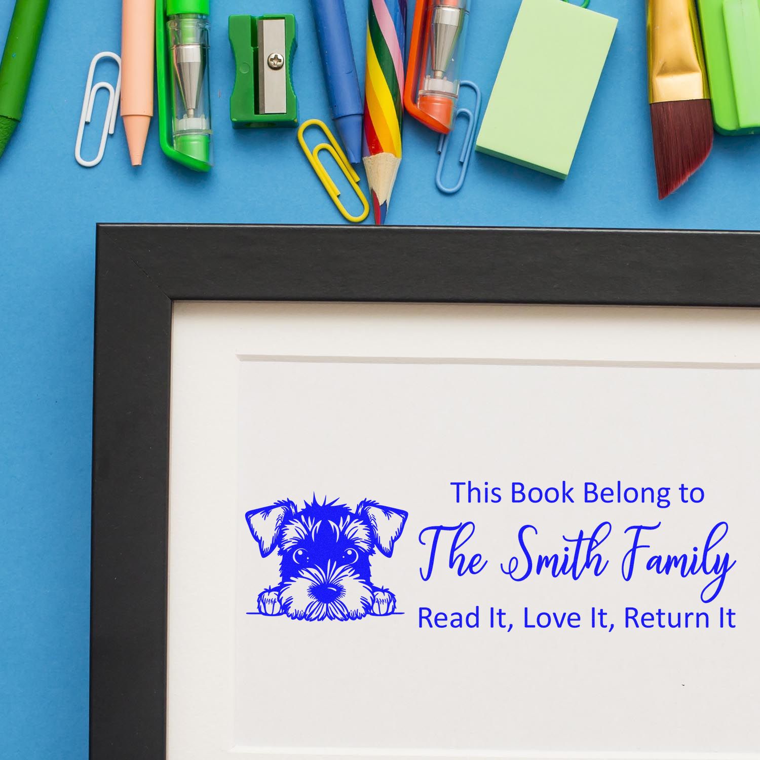 Personalized blue book stamp seal with dog logo in black frame, surrounded by colorful stationery on blue background.