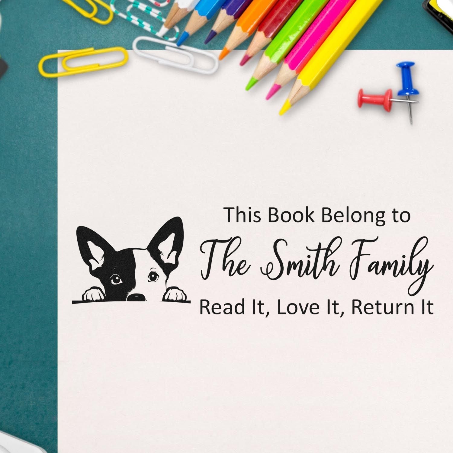 Personalized book stamp with black dog, The Smith Family text, and colorful pencils, paper clips, and pushpins on white paper.