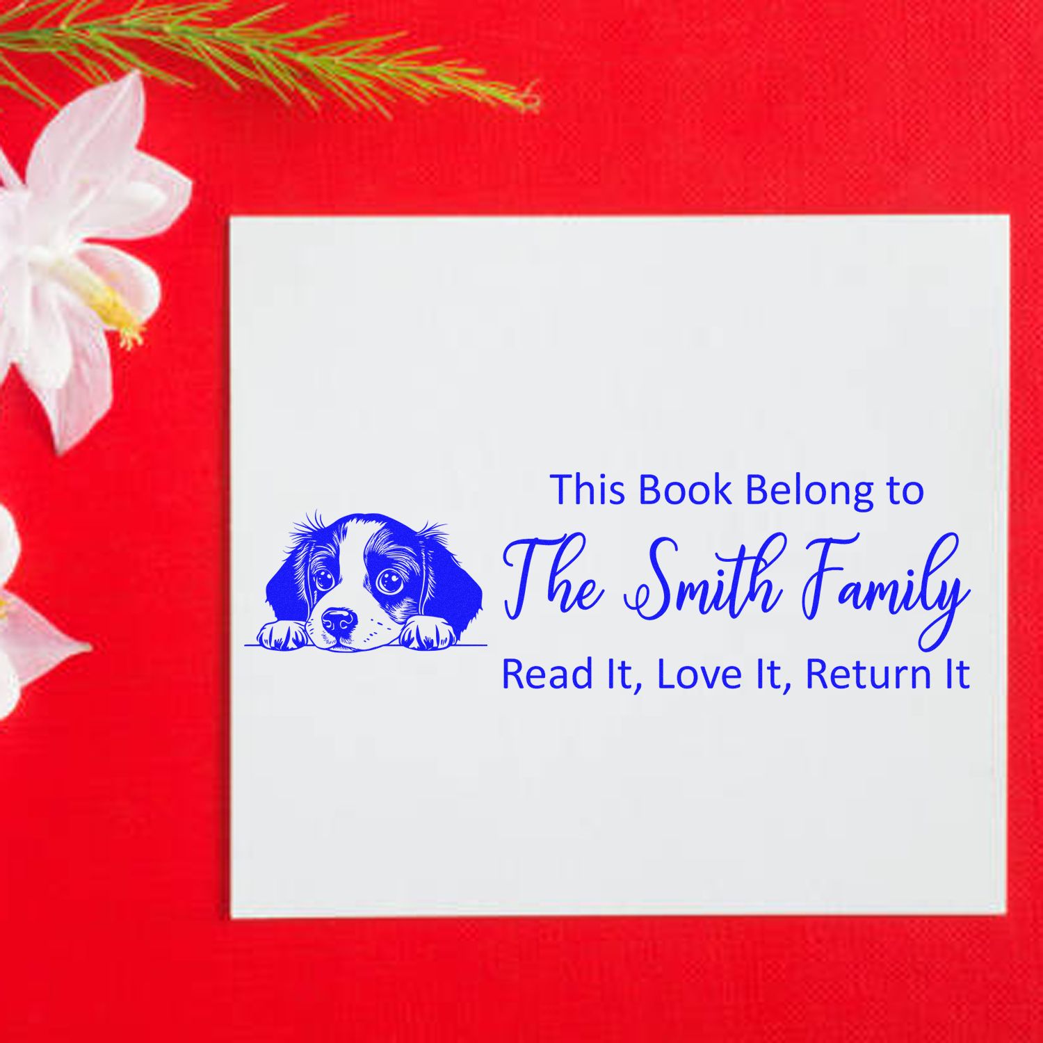 Blue custom book return stamp and seal with puppy, The Smith Family, on white square over bright red background with white flower.