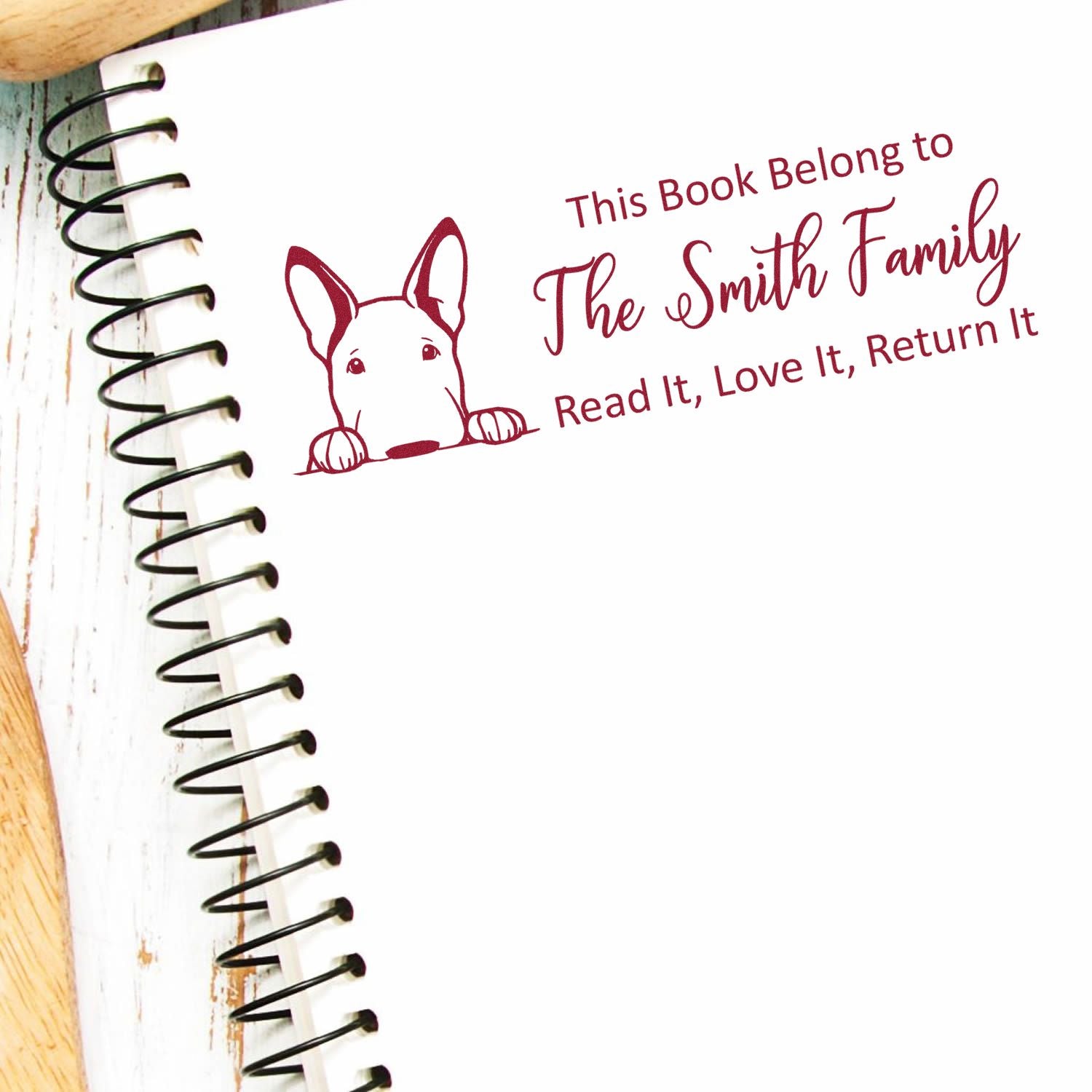 Burgundy personalized book stamp with dog, reading The Smith Family on a white spiral-bound notebook page.