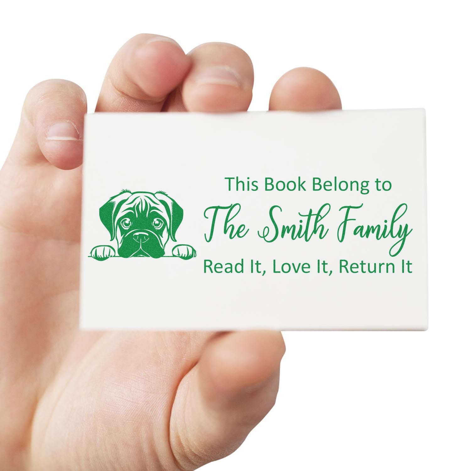 Green custom book stamp with dog seal and This Book Belongs to The Smith Family text on a white card held in hand.
