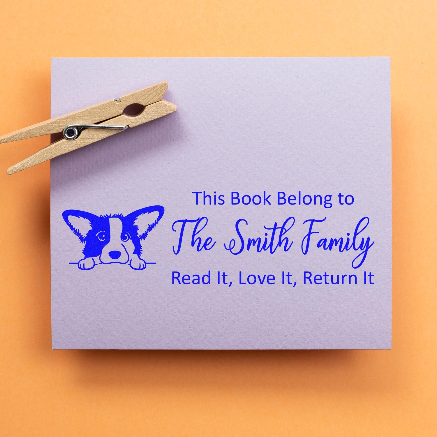 Blue custom bookplate stamp with dog seal and The Smith Family text on lavender paper, clipped with a wooden clothespin.
