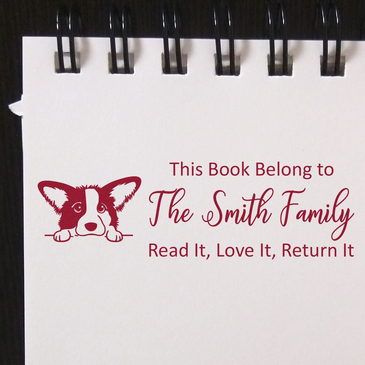 Maroon custom book stamp and seal with corgi logo, saying This Book Belongs to The Smith Family on white paper.