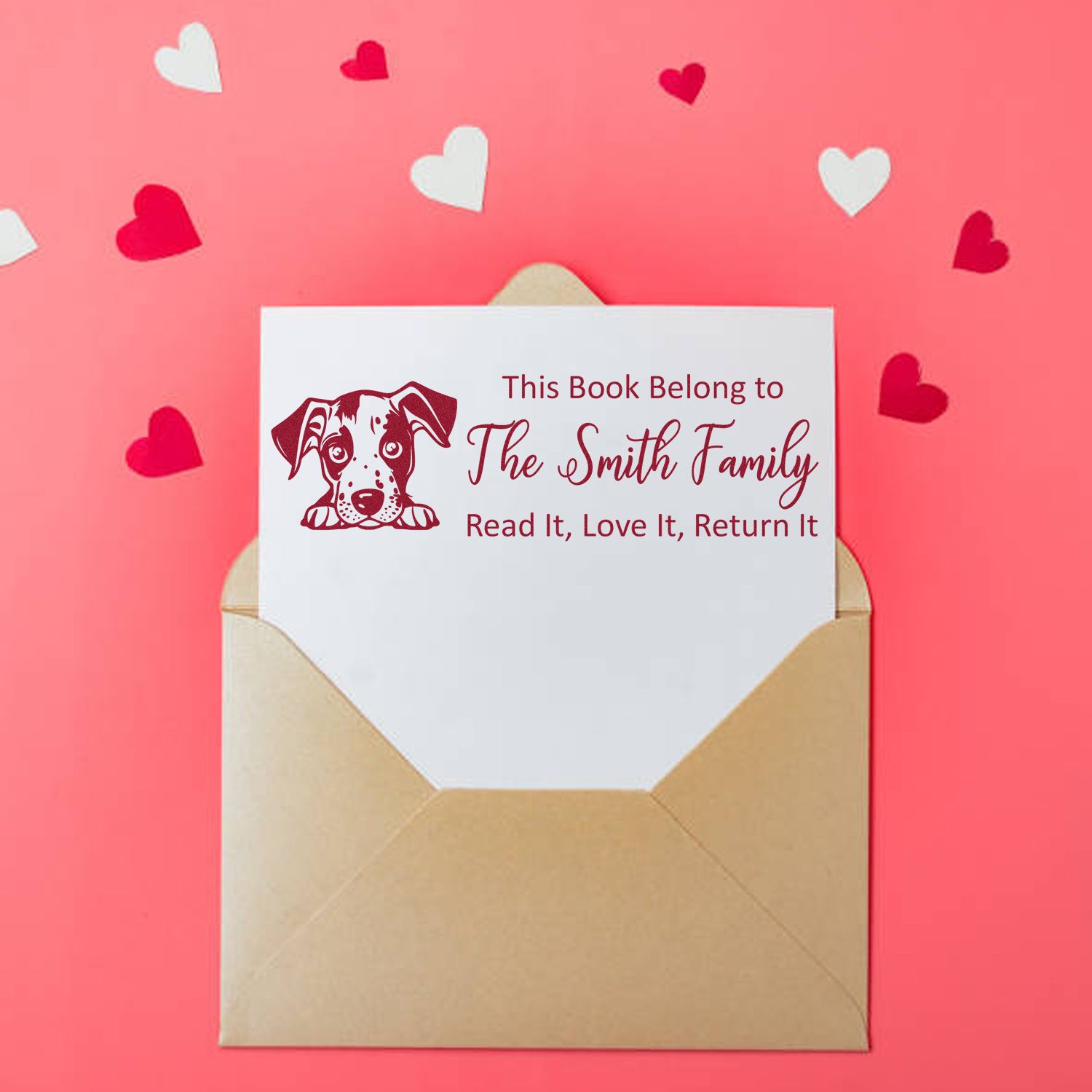 Personalized red dog book plate stamp and seal in a tan envelope on pink background with heart confetti.