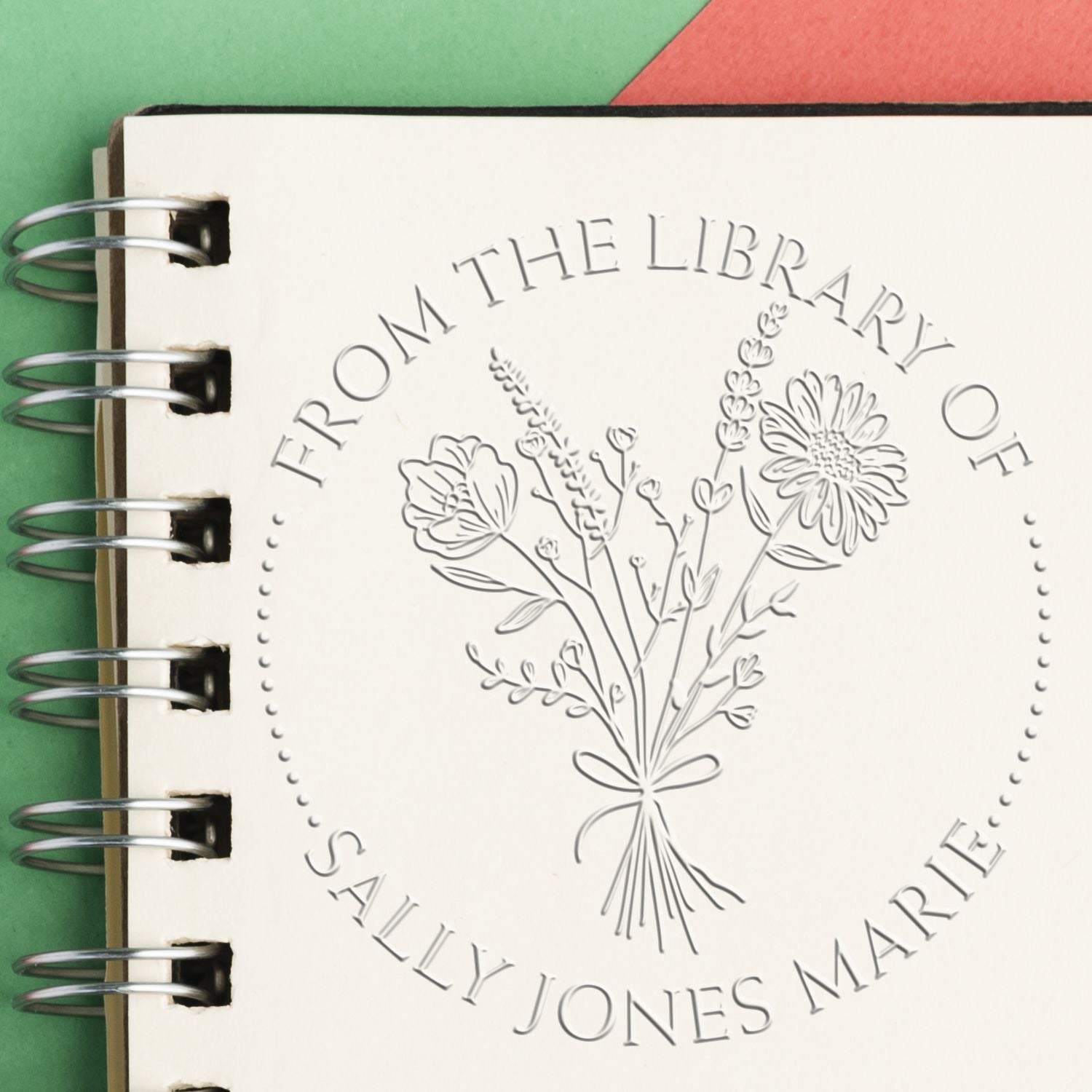 Embossed custom stamp seal on cream spiral notebook, featuring floral bouquet and “From the Library of Sally Jones Marie” text.