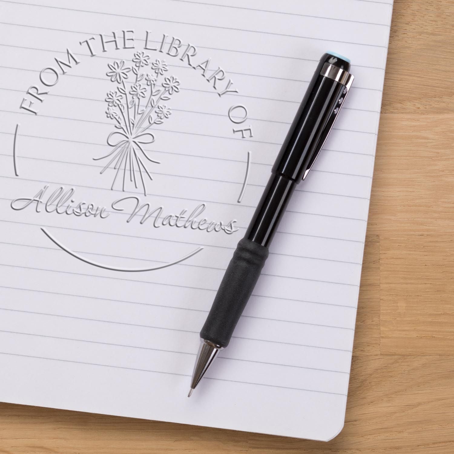 Personalized library embosser stamp and seal on lined paper, with floral design, black pen, and name Allison Mathews.