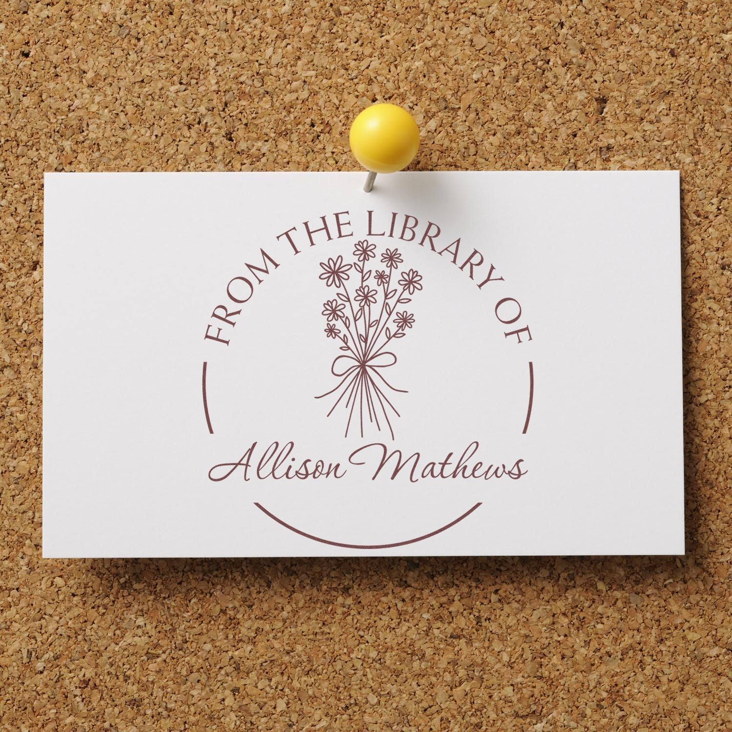 Custom library stamp seal on white card, brown floral design and From the Library of Allison Mathews, pinned to corkboard with yellow tack.