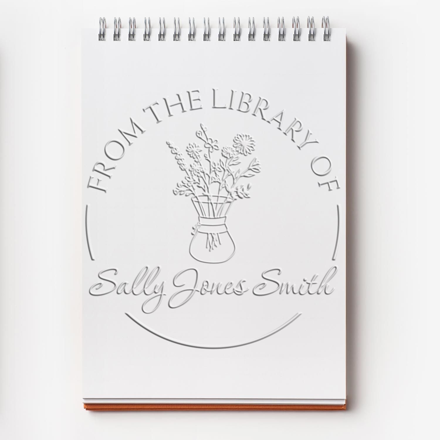 White spiral notebook with embossed library book stamp seal, floral vase emblem, and Sally Jones Smith name.